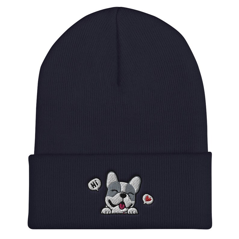 Puede incluir: Un gorro de punto azul marino con un perro de dibujos animados bordado en blanco y gris que lleva un coraz&oacute;n rojo. El perro dice "Hola" en un globo de di&aacute;logo.