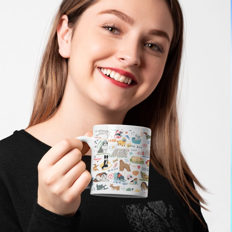 May include: White ceramic mug with a colorful illustration of dogs, bones, and dog-related words. The mug has a black handle.