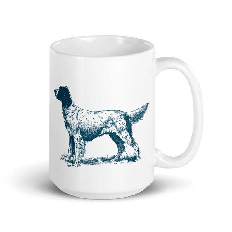 May include: White ceramic mug with a blue and white illustration of a dog. The dog is standing on its hind legs with its head turned to the side. The mug has a large handle.