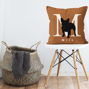 May include: A brown throw pillow with a white letter M and a black silhouette of a French Bulldog. The pillow has the name "Milo" printed in white below the silhouette.