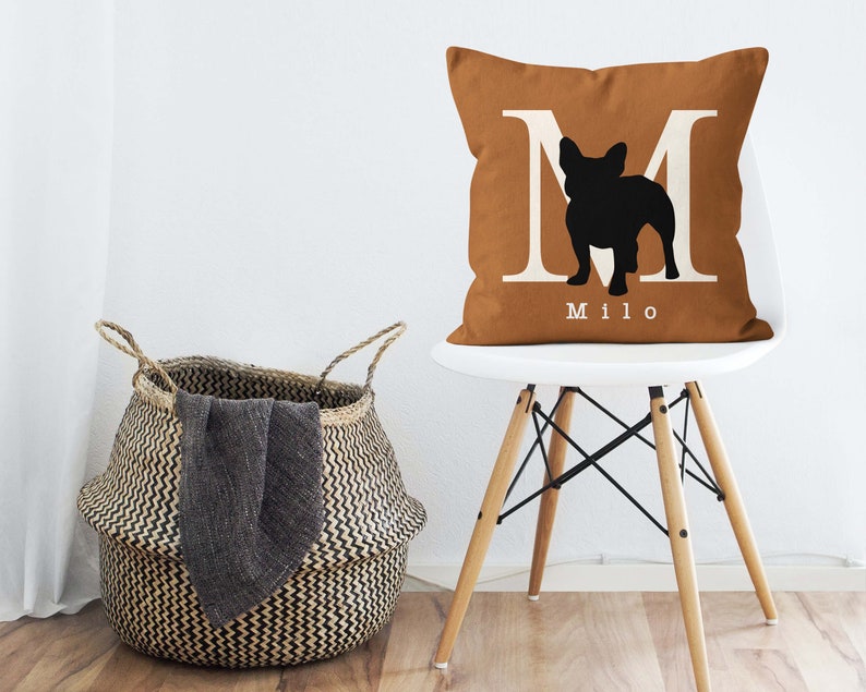 May include: A brown throw pillow with a white letter M and a black silhouette of a French Bulldog. The pillow has the name "Milo" printed in white below the silhouette.