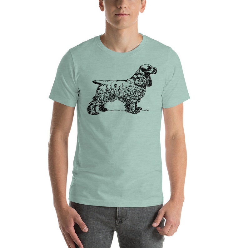 May include: A light green t-shirt featuring a black illustration of a Cocker Spaniel dog. The dog is depicted in a side profile, showcasing its distinctive long ears and fluffy fur. The t-shirt is a solid color, providing a neutral backdrop for the detailed dog graphic.