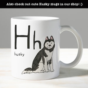 Może przedstawiać: Biały kubek ceramiczny z czarno-białym rysunkiem psa husky. Kubek ma literę "H" i napis "husky" na nim.