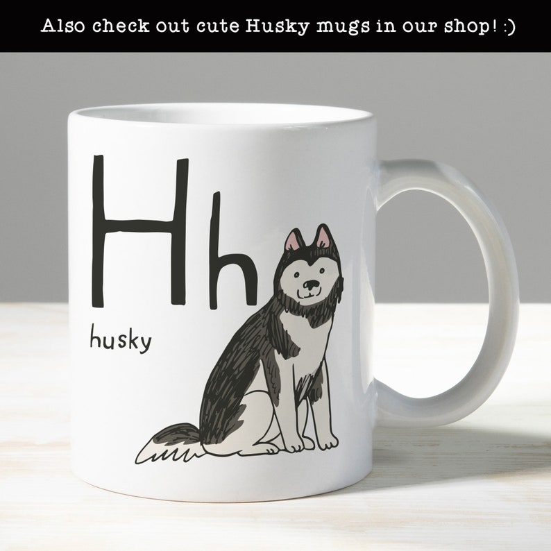 Może przedstawiać: Biały kubek ceramiczny z czarno-białym rysunkiem psa husky. Kubek ma literę "H" i napis "husky" na nim.