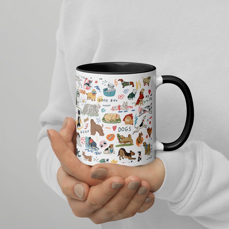 Op de afbeelding: Een witte keramische koffiemok met een zwarte rand en handvat. De mok heeft een kleurrijke illustratie van verschillende hondenrassen, waaronder een teckel, een poedel, een golden retriever en een bulldog. De illustratie bevat ook de woorden "Good Boy", "Woof" en "Dogs".