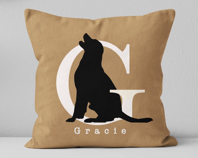 K&ouml;nnte beinhalten: Ein braunes Kissen mit einem wei&szlig;en Buchstaben G und einer schwarzen Silhouette eines Hundes, der im Buchstaben sitzt. Der Name "Gracie" ist unter dem Buchstaben gedruckt.