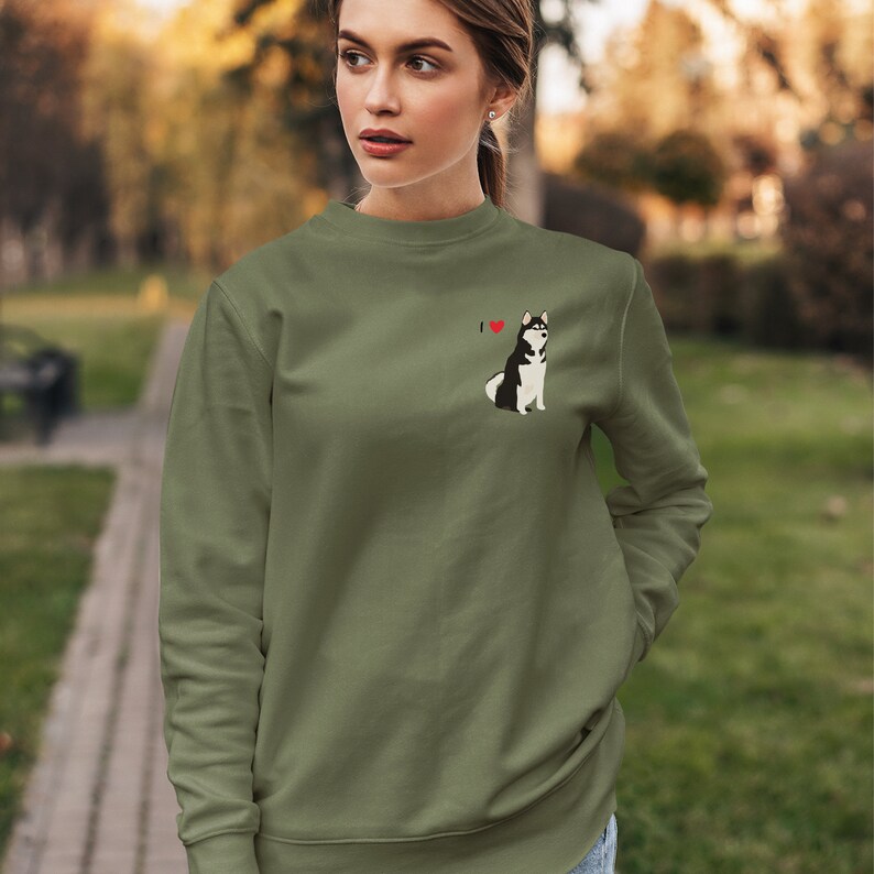 Może przedstawiać: Zielona bluza z małym haftowanym obrazkiem husky i tekstem "I &hearts;" na lewej piersi.