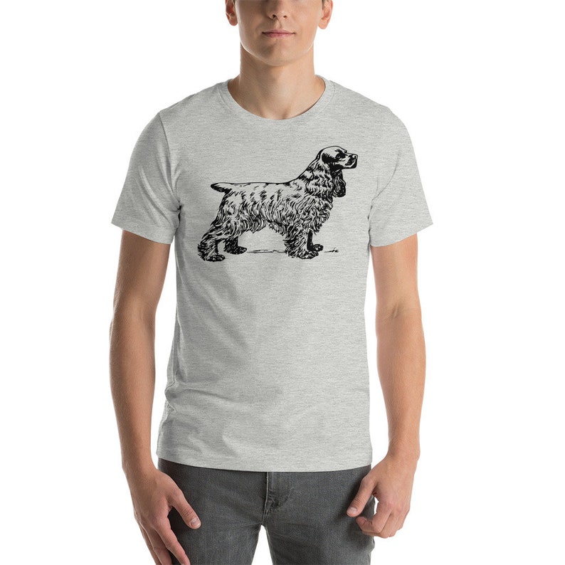 May include: A light gray t-shirt featuring a black illustration of a Cocker Spaniel dog. The dog is depicted in a side profile, showcasing its distinctive long ears and fluffy fur. The shirt is made of a soft material.