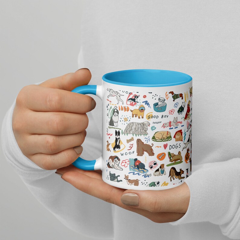 Op de afbeelding: Een witte keramische mok met een blauwe rand heeft een kleurrijke illustratie van verschillende hondenrassen, waaronder een dalmati&euml;r, een poedel, een golden retriever en een mops. De tekst "GOOD BOY", "WOOF" en "DOGS" is opgenomen in het ontwerp.