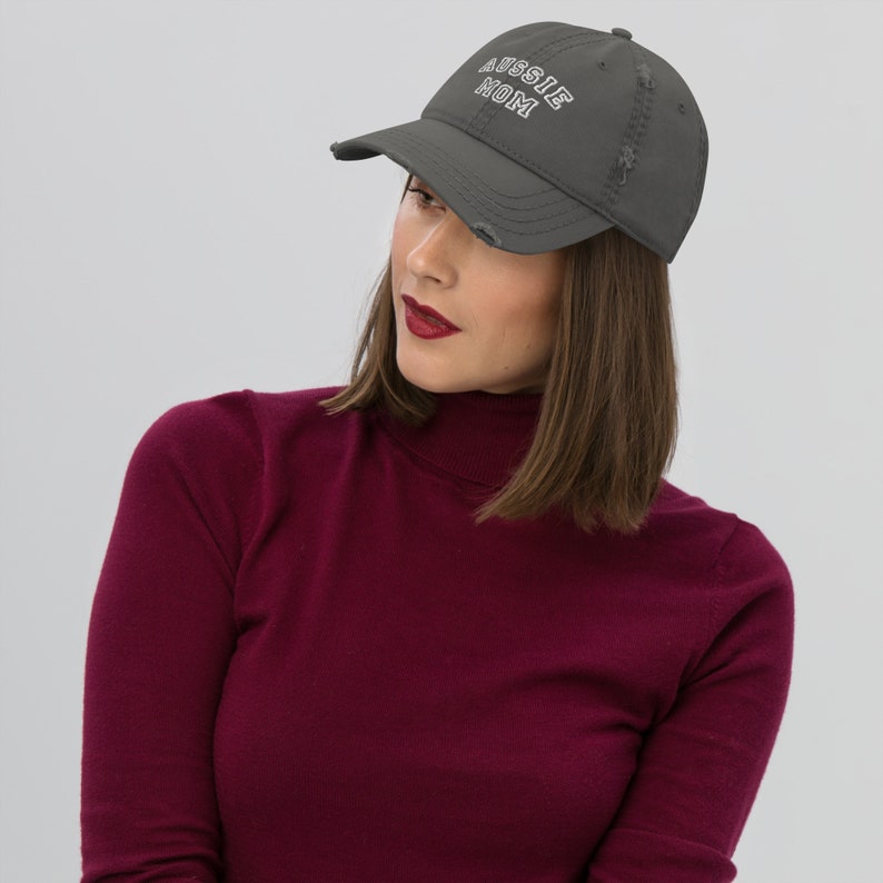 May include: A gray distressed baseball cap with white embroidered text that reads "Aussie Mom".