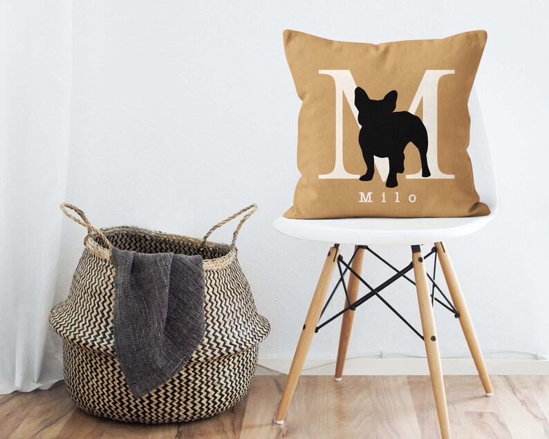 May include: A tan throw pillow with a white letter M and a black silhouette of a French Bulldog. The pillow has the name "Milo" printed on it.