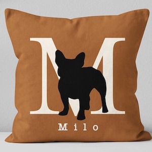 May include: A brown throw pillow with a white letter M and a black silhouette of a French Bulldog. The pillow has the name "Milo" printed in white below the silhouette.
