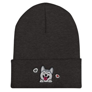 K&ouml;nnte beinhalten: Eine dunkelgraue M&uuml;tze mit einem wei&szlig;en gestickten Husky-Hund mit herausgestreckter rosa Zunge. Der Hund sagt "Hallo" in einer Sprechblase und hat ein rotes Herz in einer anderen Sprechblase.