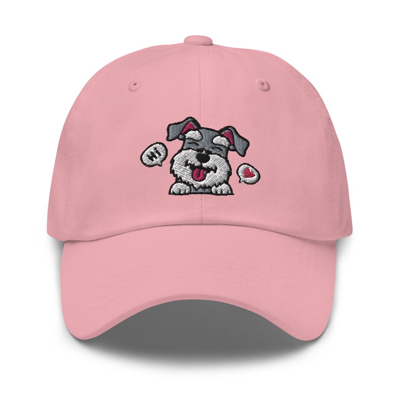 K&ouml;nnte beinhalten: Eine rosafarbene Baseballkappe mit einem gestickten Cartoon-Bild eines grau-wei&szlig;en Zwergschnauzers mit herausgestreckter Zunge. Der Hund tr&auml;gt ein rotes Herz und eine Sprechblase mit der Aufschrift "Hallo".