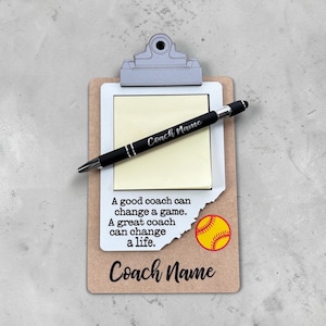 May include: A brown clipboard with a silver metal clip holding a white notepad with the text A good coach can change a game. A great coach can change a life. and a yellow softball graphic. A black pen labeled Coach Name rests on the notepad.