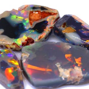 May include: Four pieces of rough opal, showing a variety of colors and patterns, including black, blue, green, orange, and red.