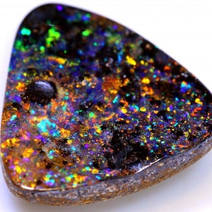 Könnte beinhalten: Ein polierter, dreieckiger schwarzer Opal-Edelstein mit lebendigen, mehrfarbigen Blitzen in Grün, Blau, Gelb und Orange. Die Oberfläche des Opals hat ein gesprenkeltes Aussehen, das sein einzigartiges Farbspiel zeigt. Die Kanten sind dunkelbraun.