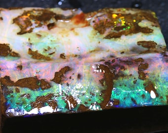 May include: A rough, rectangular piece of opal with a variety of colors, including green, blue, pink, and white. The opal is set in a brown matrix.