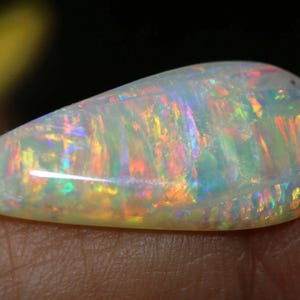 Pu&ograve; includere: Una gemma di opale a forma di goccia, con una base bianco latte. L'opale mostra vivaci lampi di colore, tra cui rosso, arancione, giallo, verde e blu, creando un effetto iridescente. La gemma &egrave; liscia e lucidata.