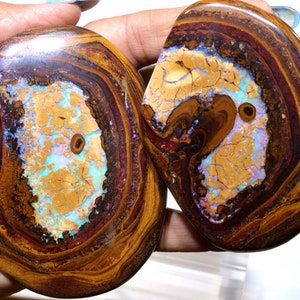 Könnte beinhalten: Zwei ovale Stücke Opal mit einer braunen, orangen und violetten Matrix. Der Opal hat einen hellblauen und weißen irisierenden Schimmer.