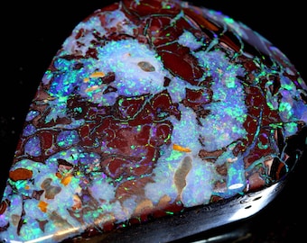 May include: A teardrop-shaped opal gemstone with a dark red base and a swirling pattern of blue, green, and white iridescent colors.