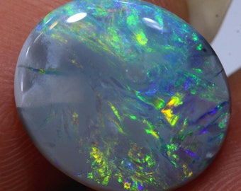 May include: A grey opal gemstone with green, blue and yellow iridescent flashes. The opal is oval shaped and has a smooth, polished surface.