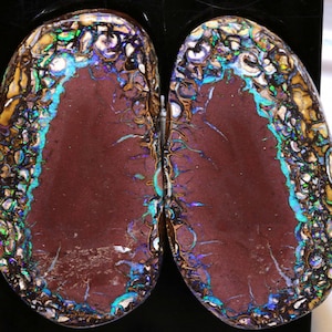 Könnte beinhalten: Zwei ovale Opal-Cabochons mit brauner Basis und einem bunten, irisierenden Rand. Die Opale haben ein einzigartiges Muster aus Blau, Grün und Gold.