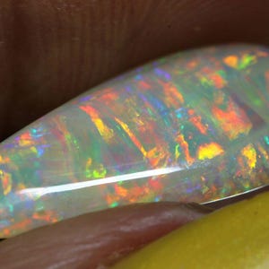 Pu&ograve; includere: Una gemma di opale a forma di goccia, con un colore di base bianco latte. L'opale mostra un vibrante gioco di colori con lampi di arancione, giallo, verde e blu. La gemma &egrave; lucidata e liscia, mettendo in risalto la sua bellezza naturale.