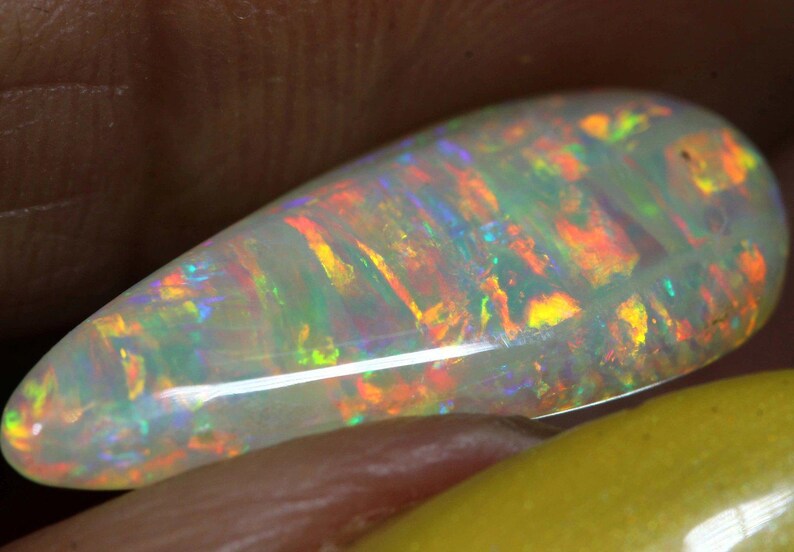 Pu&ograve; includere: Una gemma di opale a forma di goccia, con un colore di base bianco latte. L'opale mostra un vibrante gioco di colori con lampi di arancione, giallo, verde e blu. La gemma &egrave; lucidata e liscia, mettendo in risalto la sua bellezza naturale.