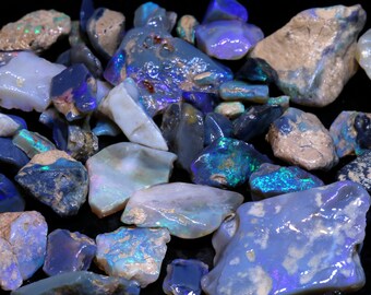 Puede incluir: Una colección de piedras de ópalo en bruto sin pulir en varios tonos de azul, verde y blanco. Las piedras son de forma y tamaño irregulares, y algunas tienen un brillo iridiscente.