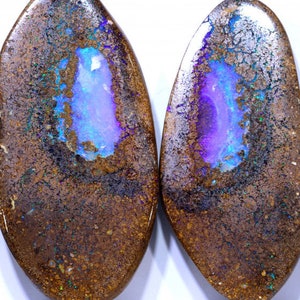 Könnte beinhalten: Zwei ovale Opale mit brauner Matrix und einem leuchtend blauen und violetten, irisierenden Schimmer.