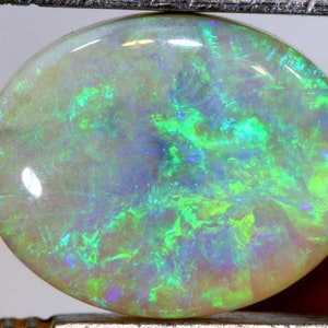 May include: A white opal gemstone with green and blue iridescent flashes. The opal is oval shaped and has a smooth, polished surface.