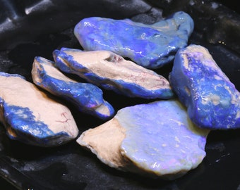 Puede incluir: Una colección de cinco piedras de ópalo en bruto con un brillo iridiscente azul y blanco. Las piedras son de varios tamaños y formas.