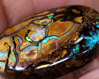 May include: A close-up of a dark brown, green, and blue opal gemstone with a black backing. The opal has a swirling pattern of colours and a smooth, polished surface.