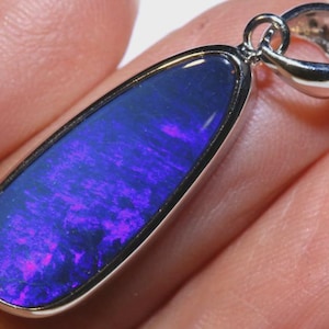 Puede incluir: Colgante de plata con ópalo en forma de lágrima. El ópalo muestra colores azules y púrpuras vibrantes. El colgante está engastado en un bisel de plata y tiene un lazo de plata para una cadena.