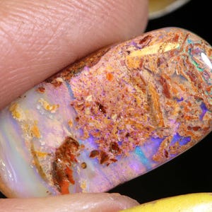 Könnte beinhalten: Ein lebendiger, ovaler Opal-Edelstein mit einem Mix aus irisierenden Farben in Pink, Orange und Blau. Der Stein hat eine raue, strukturierte Oberfläche mit braunen und weißen Einschlüssen.