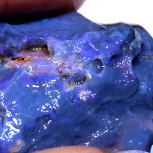 May include: A rough, blue opal with a purple and white iridescent sheen. The opal has a natural, unpolished surface.