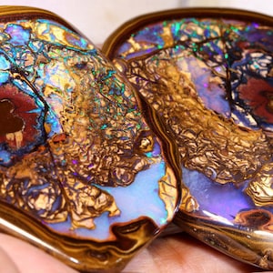 Könnte beinhalten: Zwei große, irisierende Opal-Cabochons mit einer braunen Eisenmatrix. Die Opale zeigen einen Farbschattenspiel in Blau, Grün, Lila und Rot.
