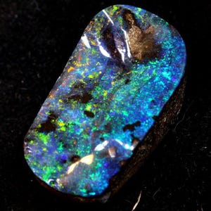 May include: A polished black opal gemstone with vibrant blue, green, and yellow flashes. The opal has a dark base color with a play of color across its surface. The stone is cut into a rounded rectangular shape.