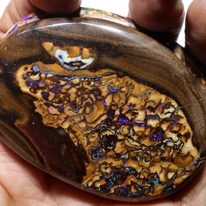 Op de afbeelding: Een grote, ovale opaal met een bruine, zwarte en witte matrix. De opaal heeft een levendige, iriserende weergave van paars, blauw en groen.