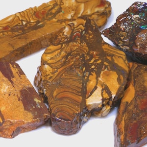 Puede incluir: Una colecci&oacute;n de piedras naturales en bruto con una variedad de colores y patrones. Las piedras muestran tonos de marr&oacute;n, naranja y rojo, con vetas y texturas &uacute;nicas. Una piedra tiene colores iridiscentes.