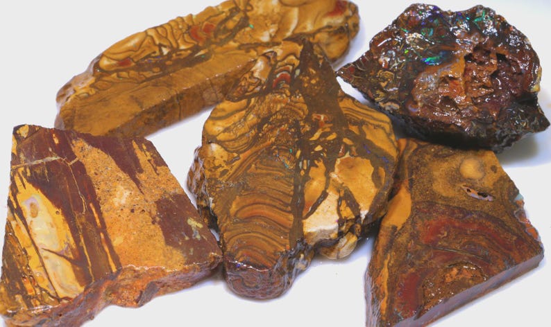 Puede incluir: Una colecci&oacute;n de piedras naturales en bruto con una variedad de colores y patrones. Las piedras muestran tonos de marr&oacute;n, naranja y rojo, con vetas y texturas &uacute;nicas. Una piedra tiene colores iridiscentes.