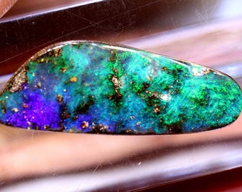 May include: A green, blue and purple opal gemstone with a gold and black matrix. The opal is a teardrop shape and is set in a clear display case.