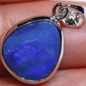 May include: A silver pendant featuring a pear-shaped blue opal. The opal has internal flashes of purple and blue. The pendant has a simple, elegant design. Ideal for adding a touch of colour to any outfit.