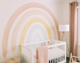 May include: A white crib with a pink blanket and stuffed animals in a nursery with a rainbow wall mural.