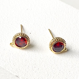 May include: A pair of gold stud earrings with red gemstone accents. The earrings have a delicate, ornate design.