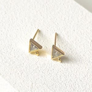 Puede incluir: Un par de pendientes de oro en forma de triángulo con piedras de circonita cúbica transparentes.