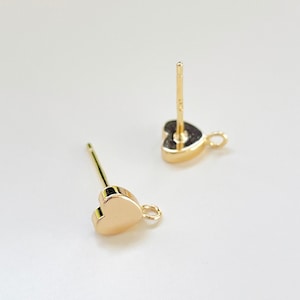 Pode incluir: Dois achados de brincos em forma de coração de ouro com um anel de salto em cada um. Os achados têm um poste para prender a um brinco.
