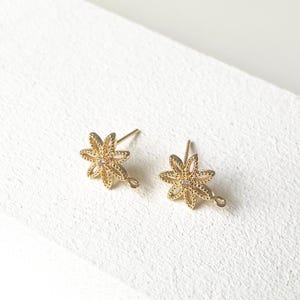 May include: A pair of gold-tone earring findings with a flower design. Each finding has a small clear rhinestone in the center of the flower.