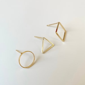 May include: Three gold-toned geometric earrings: a circle, a triangle, and a square.